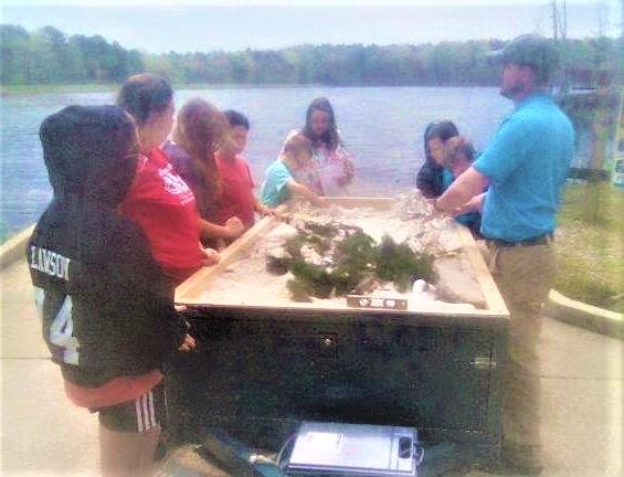 Students and presenter gathered around stream table presentation at the Eco Day at the Piney Wood Rec Area